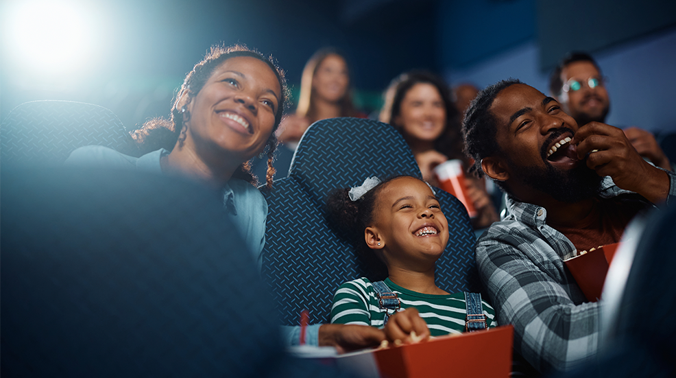 Happy black family laughing while watching funny movie at the cinema